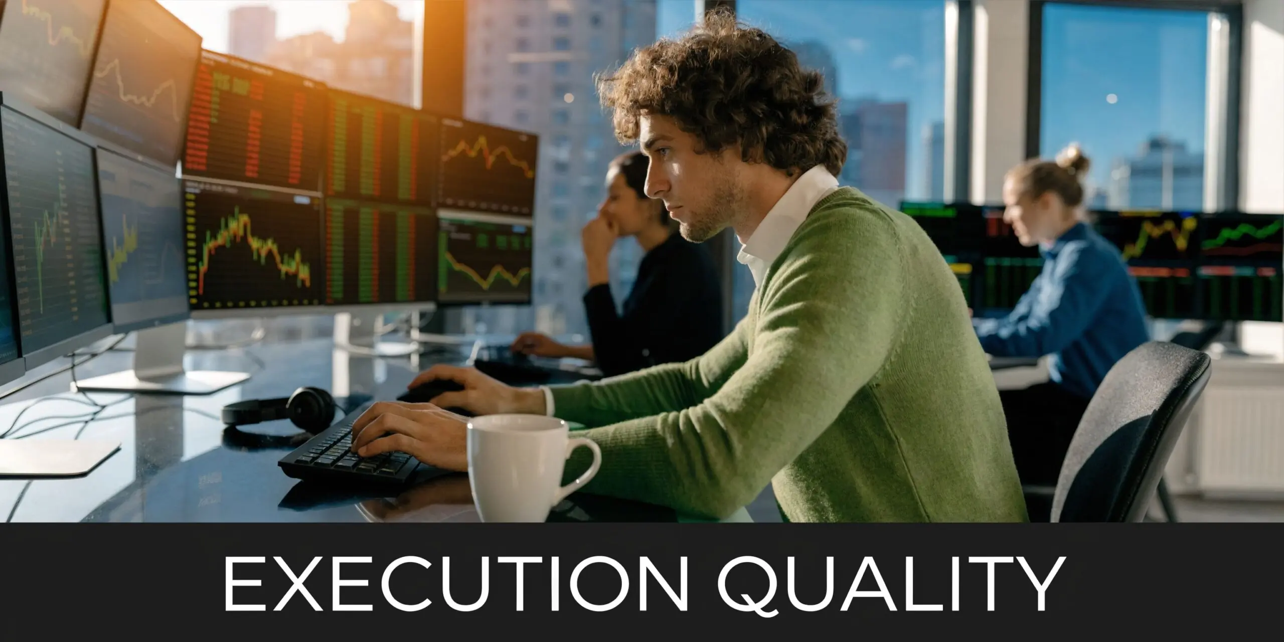 A professional trader wearing a green sweater working at a desk with multiple computer stock market monitors.