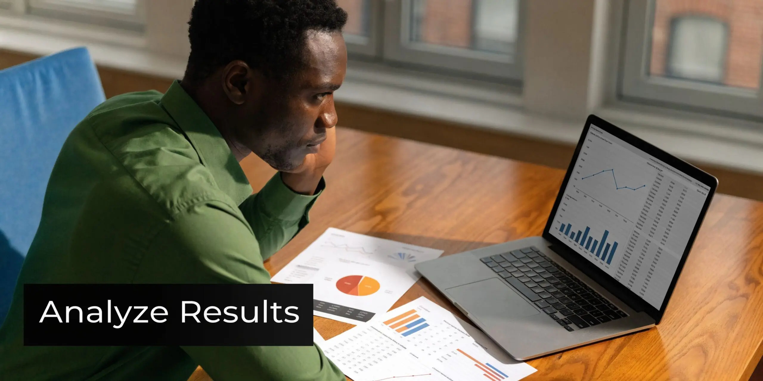 A focused man analyzing financial charts and data on a laptop screen while working at a desk.