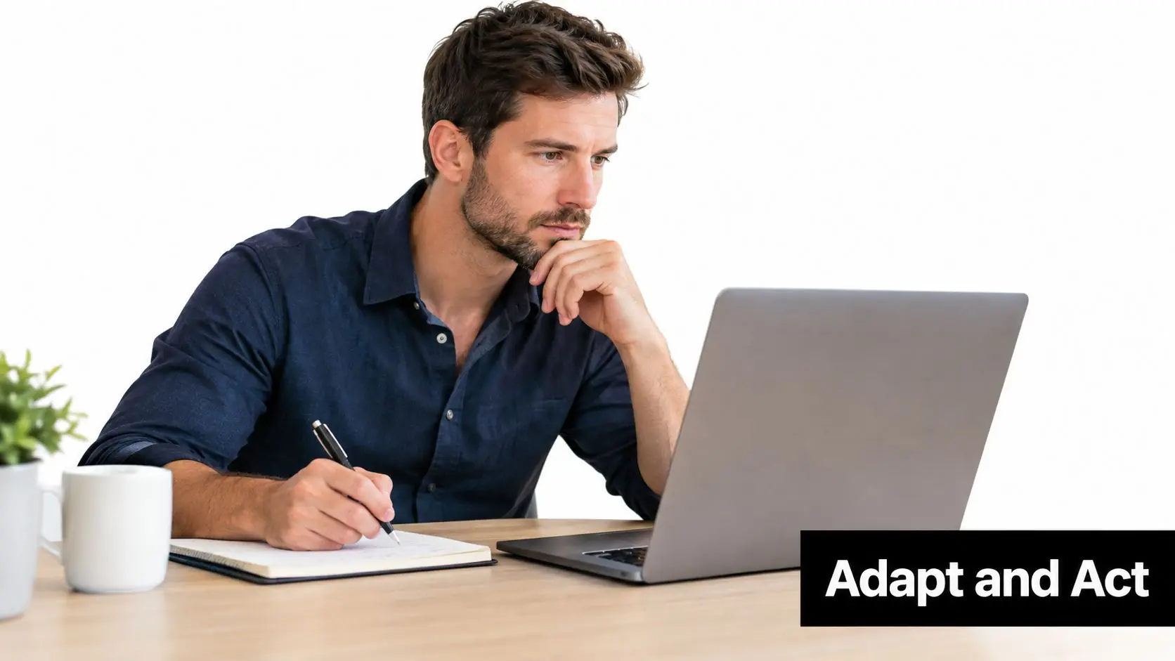 A professional man sitting at a desk with a laptop and notebook, focused on work.
